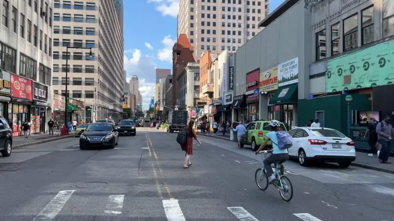 Busy street scene in Downtown Brooklyn with pedestrians, cyclists, cars, and various storefronts