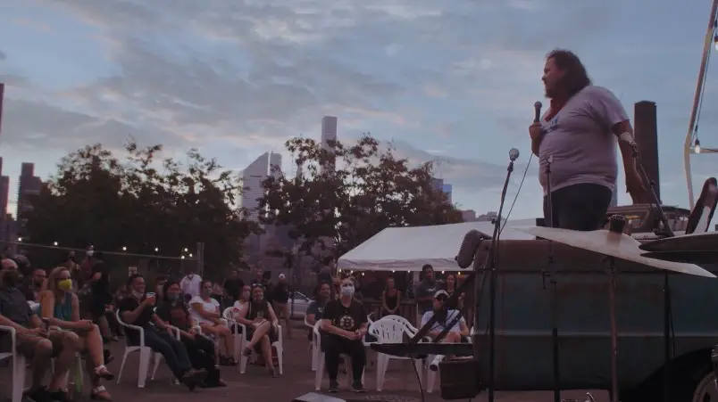 An outdoor comedian captivates a crowd under a twilight sky