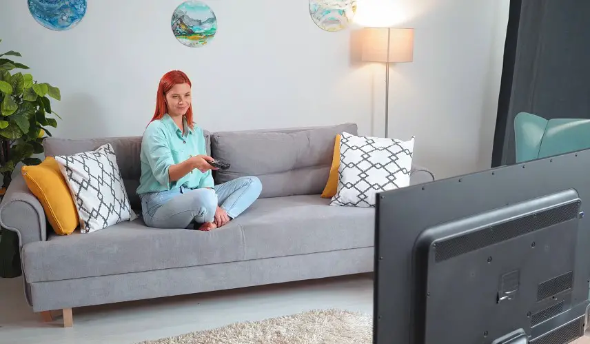 Relaxed woman sits on a gray couch, remote in hand