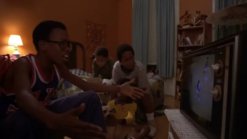 Several kids sit on the floor and watch TV together in a warm, cozy Brooklyn bedroom