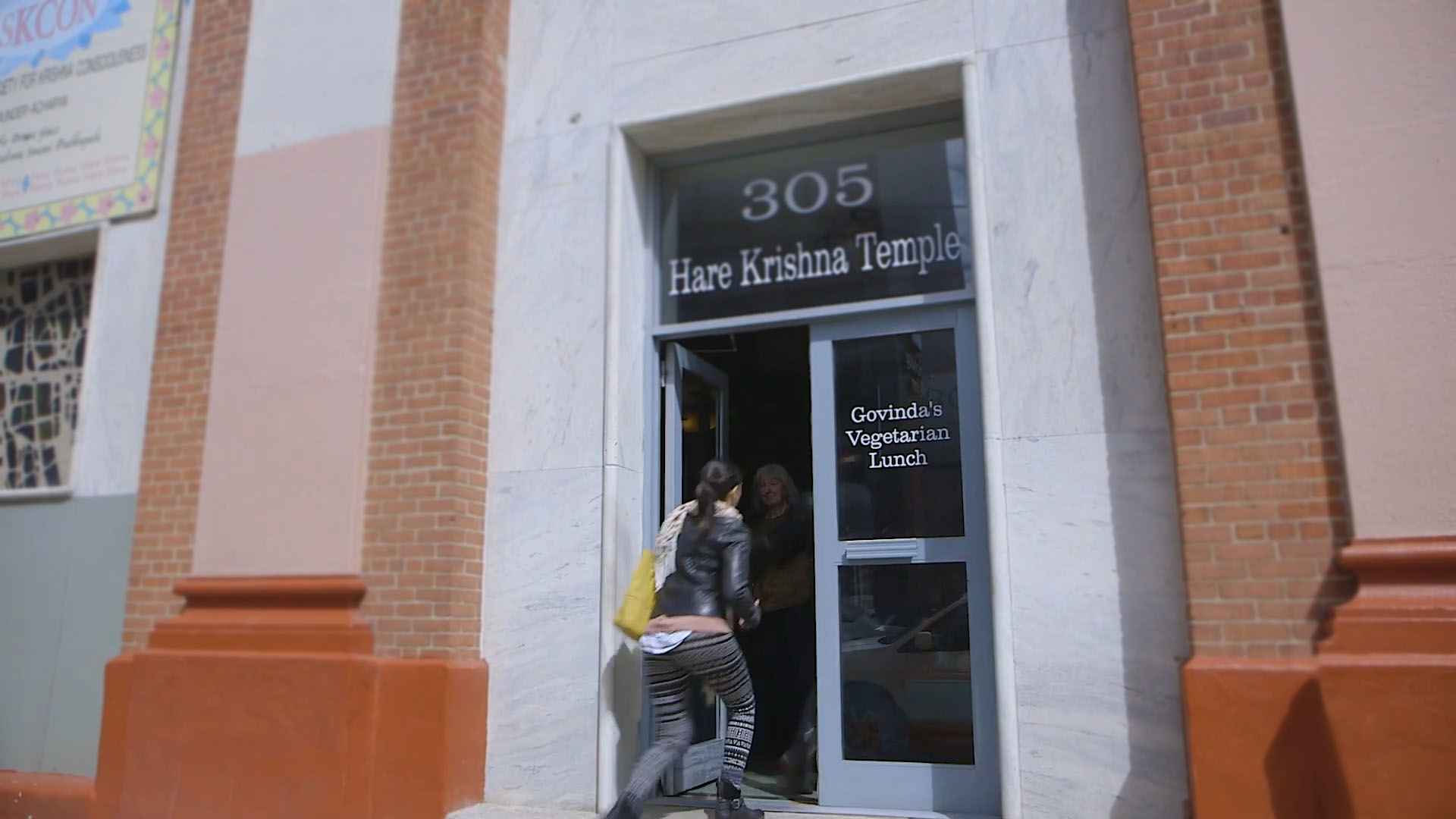 A woman entering the door of the Hare Krishna Temple in Brooklyn with the sign “Govinda’s Vegetarian Lunch