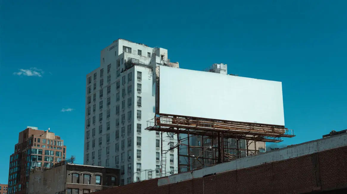Large blank billboard in Brooklyn with tall buildings in the background under a clear blue sky