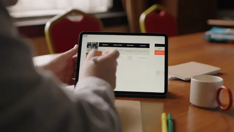 A person uses a tablet with notes and charts open on the screen at a study table
