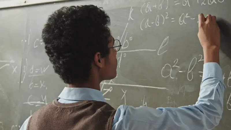 A student writes mathematical equations on a chalkboard during class