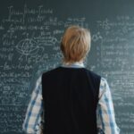 A student stands in front of a chalkboard filled with complex mathematical formulas at a university