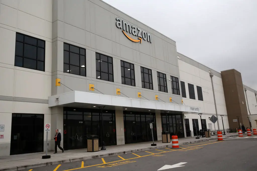 Amazon warehouse facility exterior with large logo, glass windows, and multiple entry points