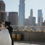 A bride and groom share a kiss on a hotel rooftop, with the New York City skyline in the background