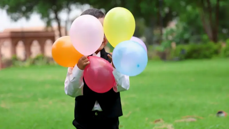 A child holding colorful balloons outdoors on a grassy field