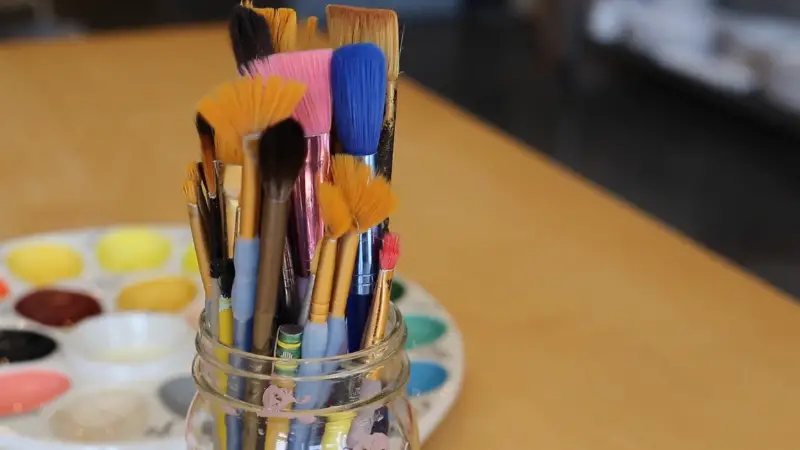 Paintbrushes in a jar with a watercolor palette on a table for an art birthday activity