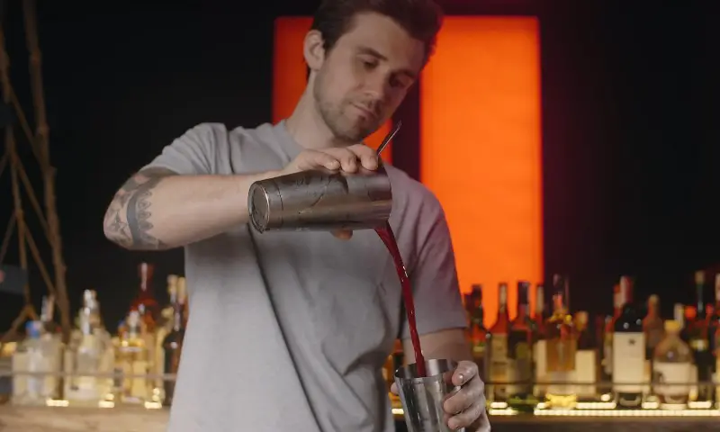 A man pours a drink into a cocktail shaker