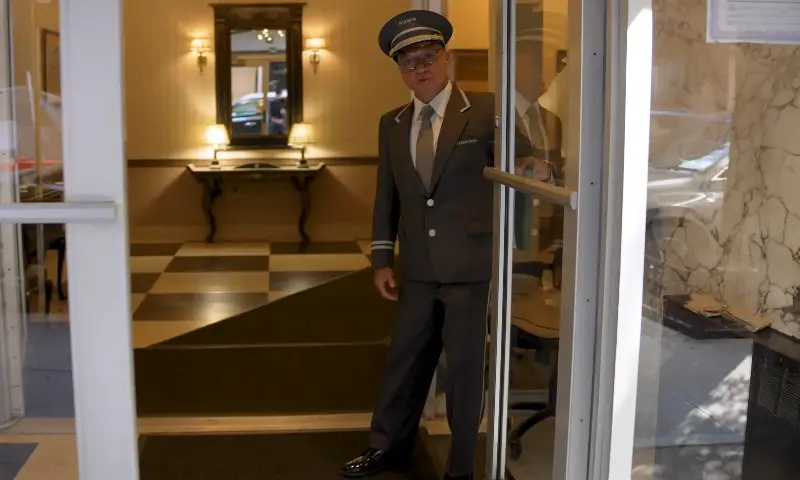 A man in a suit and tie stands in the doorway of a hotel