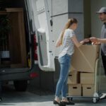 A man and woman are unloading boxes from a moving truck in a residential area