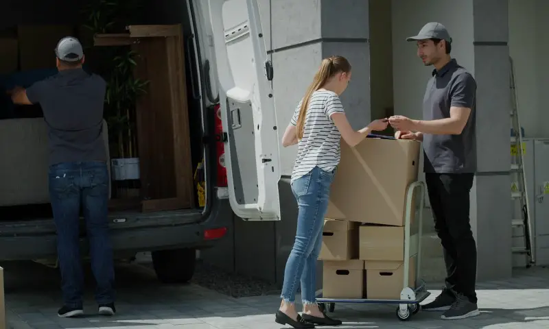 A man and woman are unloading boxes from a moving truck in a residential area
