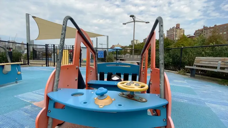 Pier 6 playground area with a boat-themed structure and blue rubber play surface in Brooklyn Bridge Park