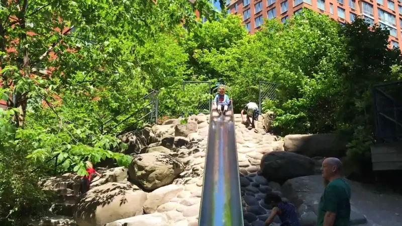 Teardrop Park with a long stone slide surrounded by greenery and kids playing