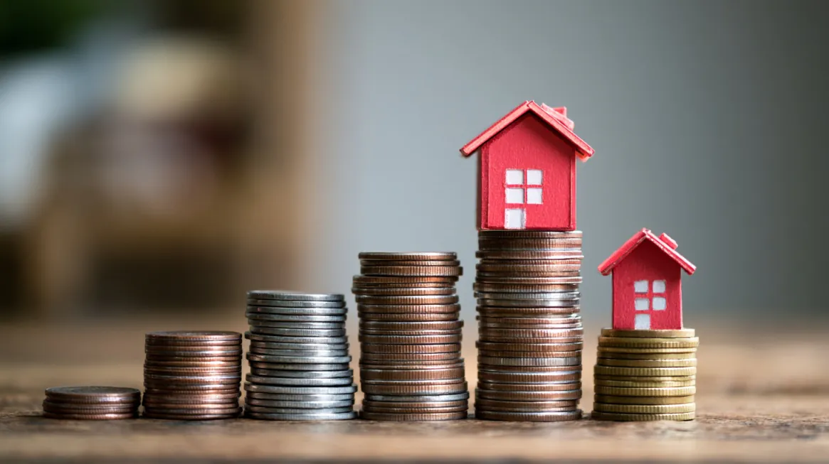 Stacks of coins arranged by height with miniature red houses on top, representing housing costs and financial planning